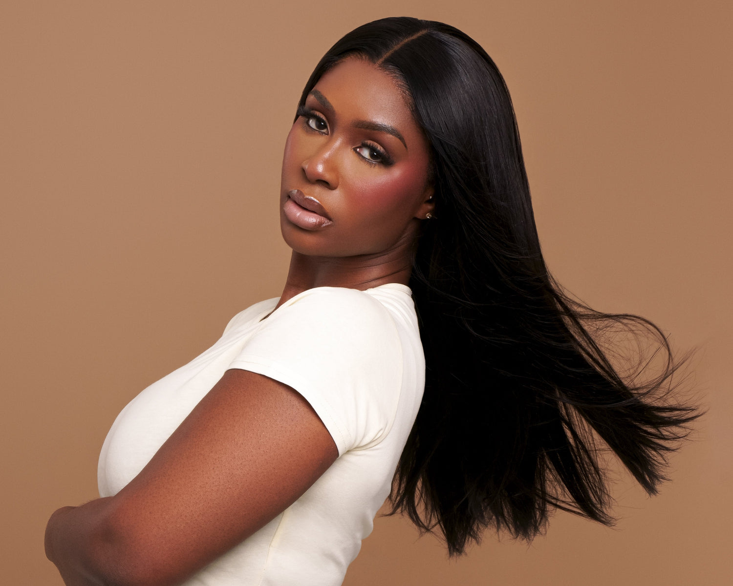 Woman with long black hair wearing a white top and dark blue pants on a brown background